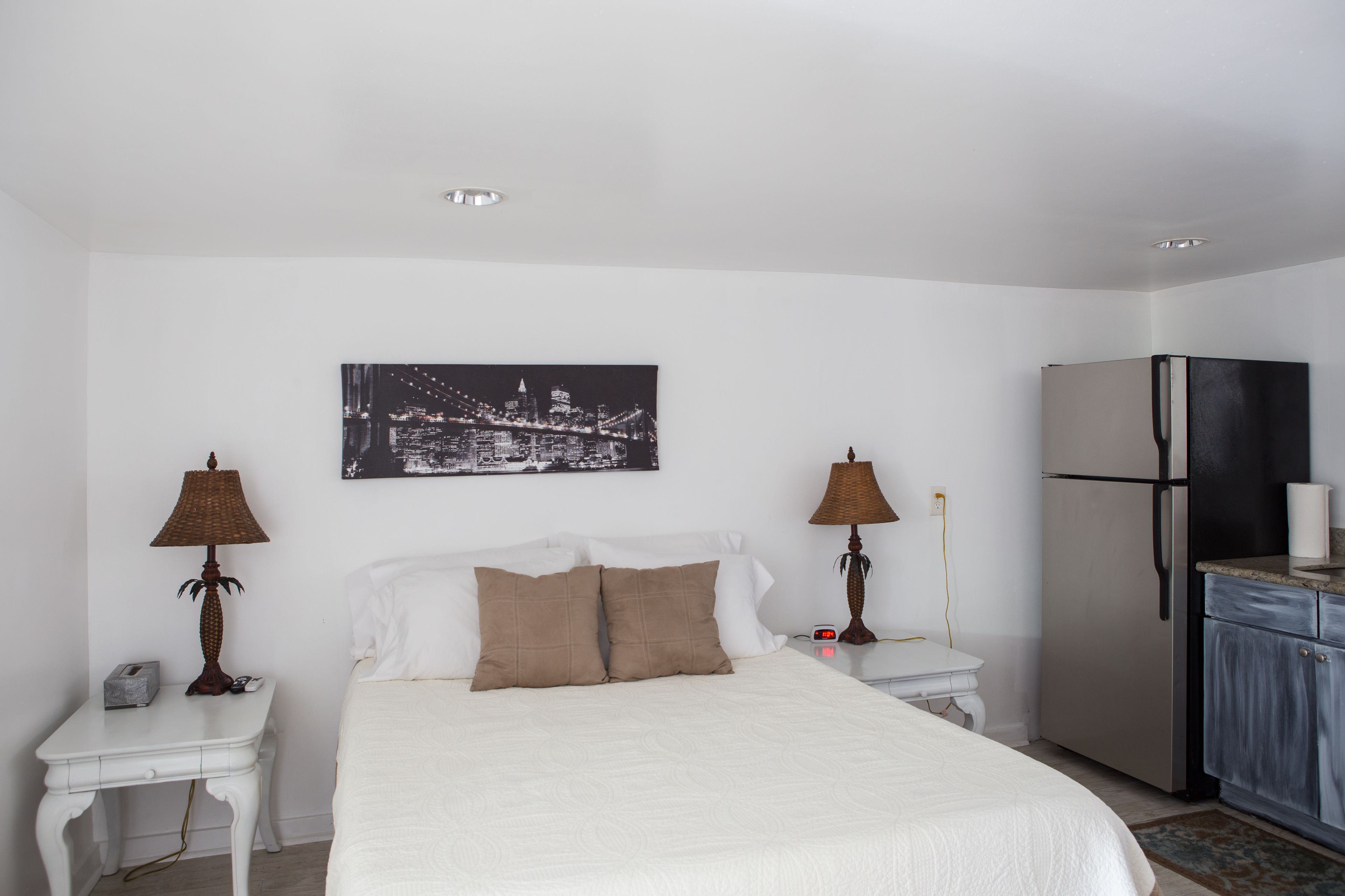 Een hotelkamer met een bed, twee nachtkastjes met lampen, een koelkast en een aan de muur hangend schilderij.