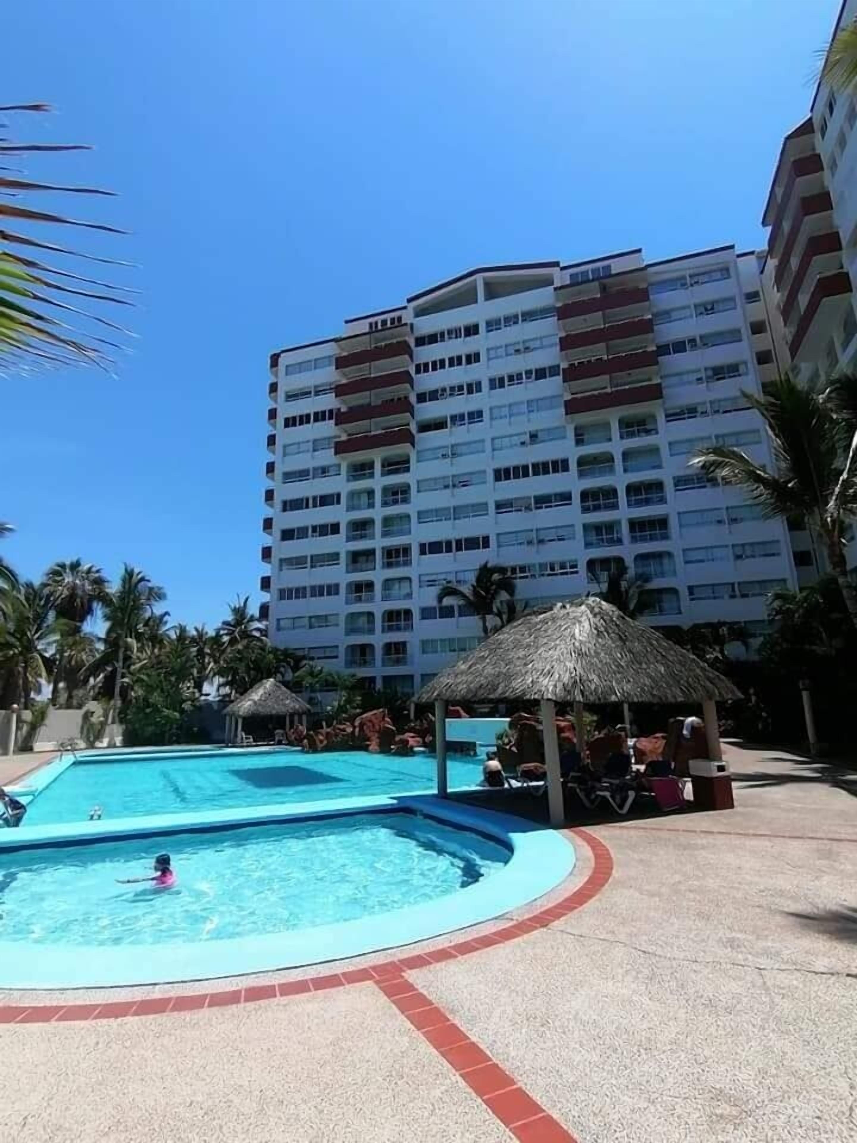 Un hôtel doté d’une grande piscine, de palmiers et d’un immeuble à plusieurs étages avec des balcons.