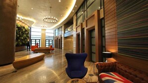 Un hall d’entrée spacieux au design moderne, comprenant un fauteuil bleu, un canapé rouge et bleu, et une table basse en bois.