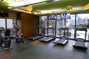 A gym with treadmills, stationary bikes, and a TV screen displaying an athlete. - HI HOME At The Knightsbridge Residences (Makati)