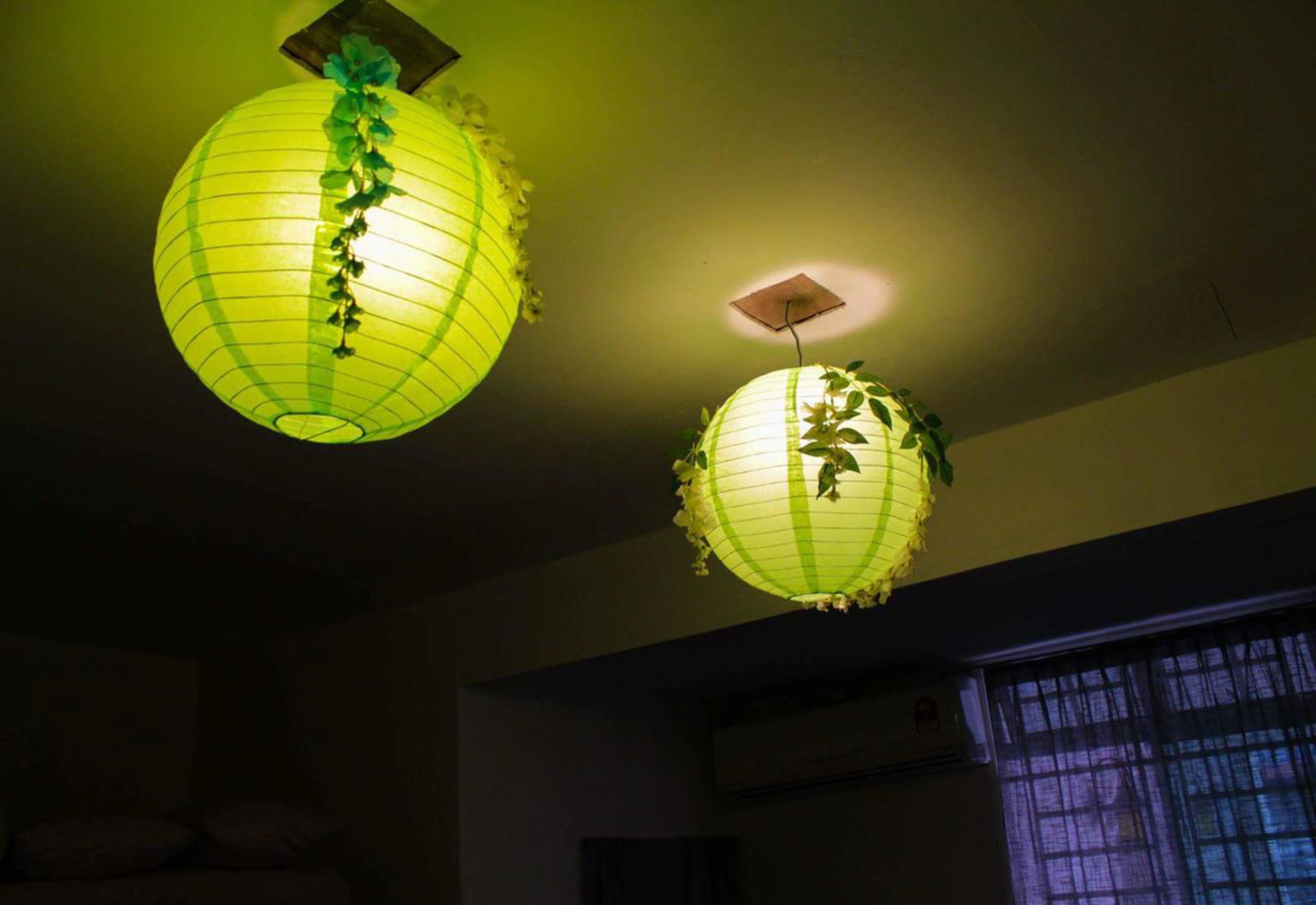 Two hanging paper lanterns with green patterns in a dimly lit room.