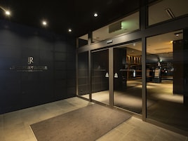 Una entrada de hotel moderna con puertas de cristal, una pared oscura con el nombre del hotel y suelo alfombrado.