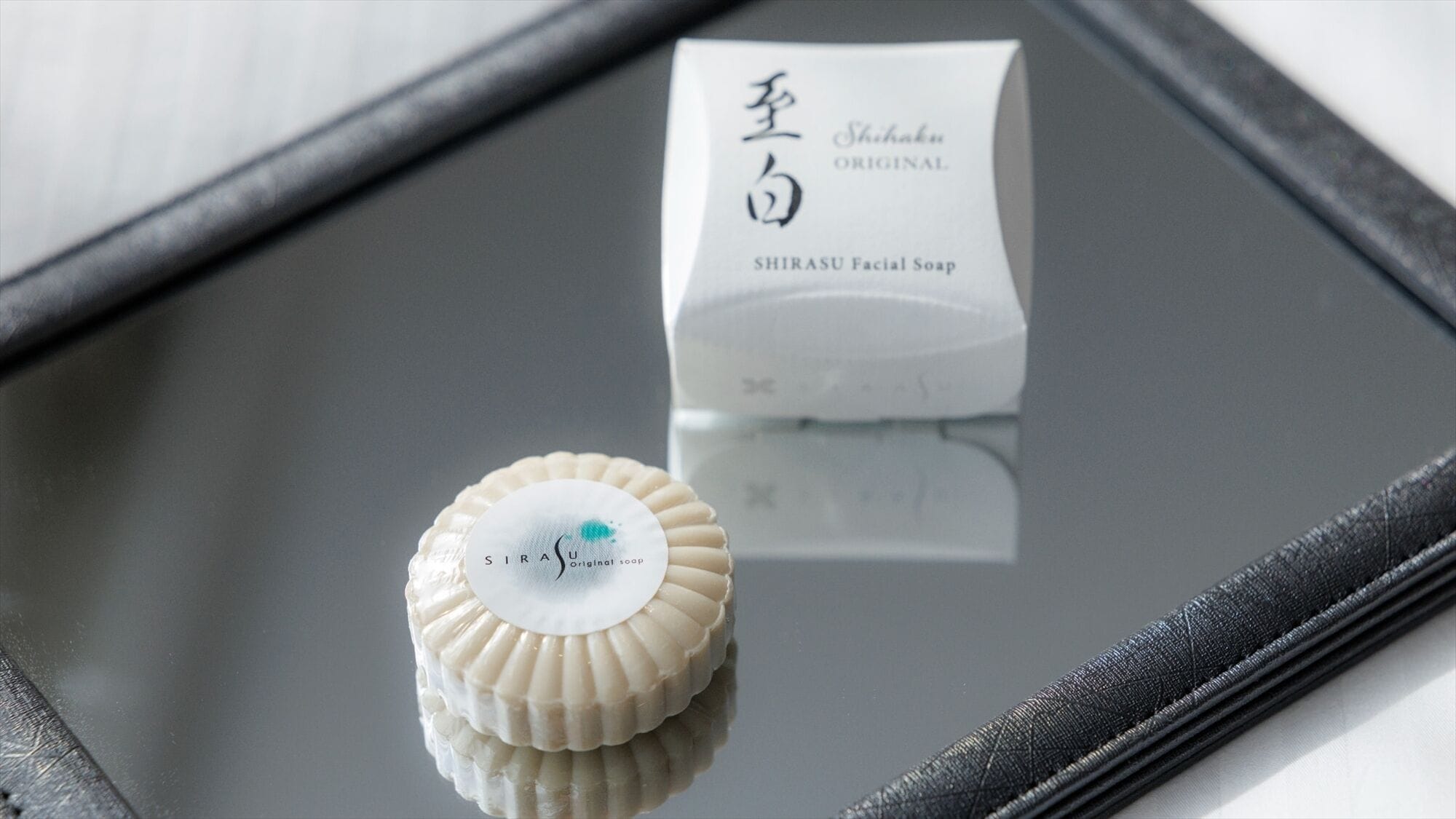 A white box labeled "Shirasu Original" and a white soap with a scalloped edge on a reflective surface.