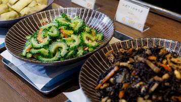 A buffet with various dishes including a bowl of sliced vegetables, a bowl of mushrooms, and a bowl of dumplings.