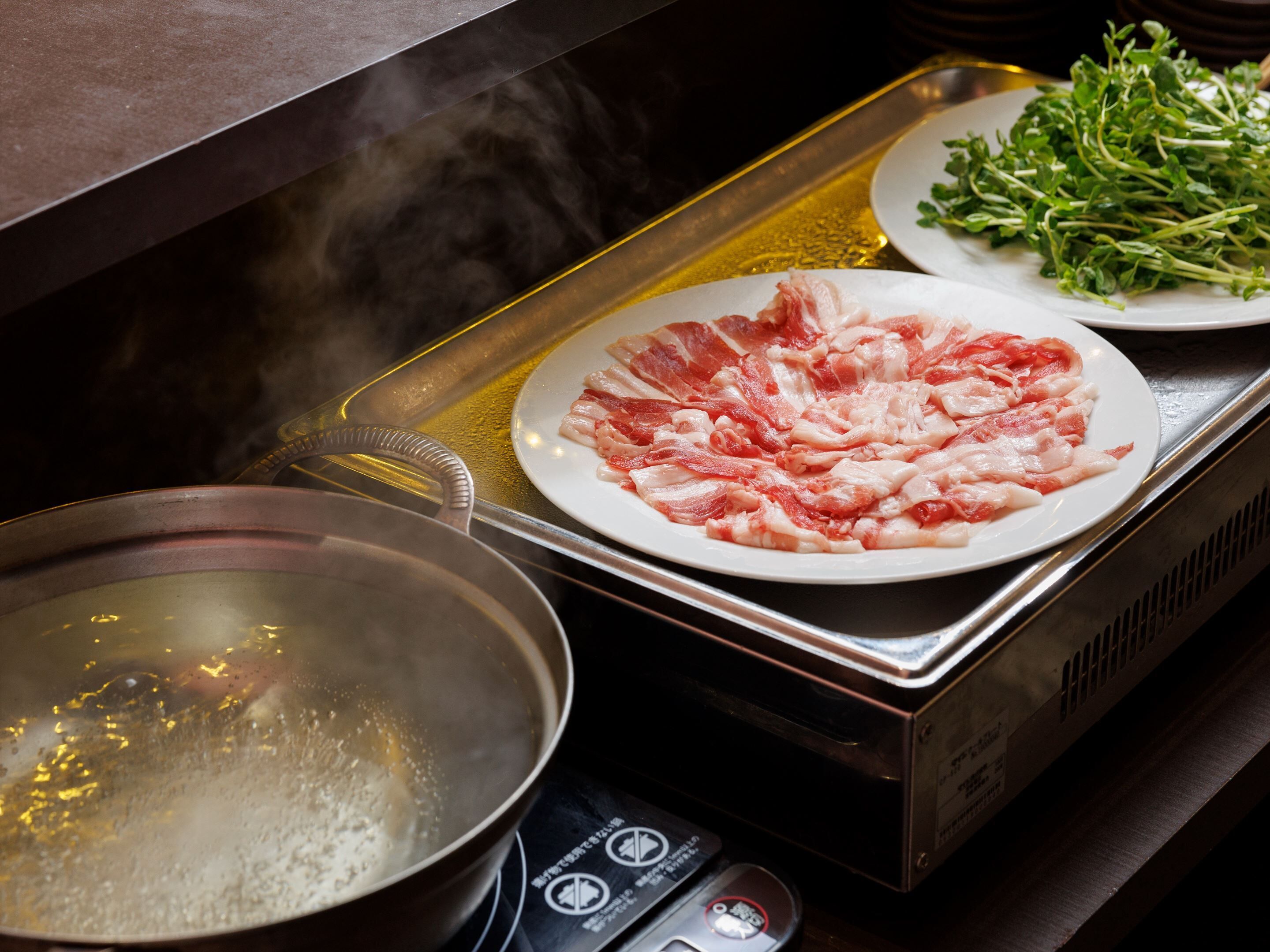 A kitchen with a stove, a pot, and a plate of raw meat.