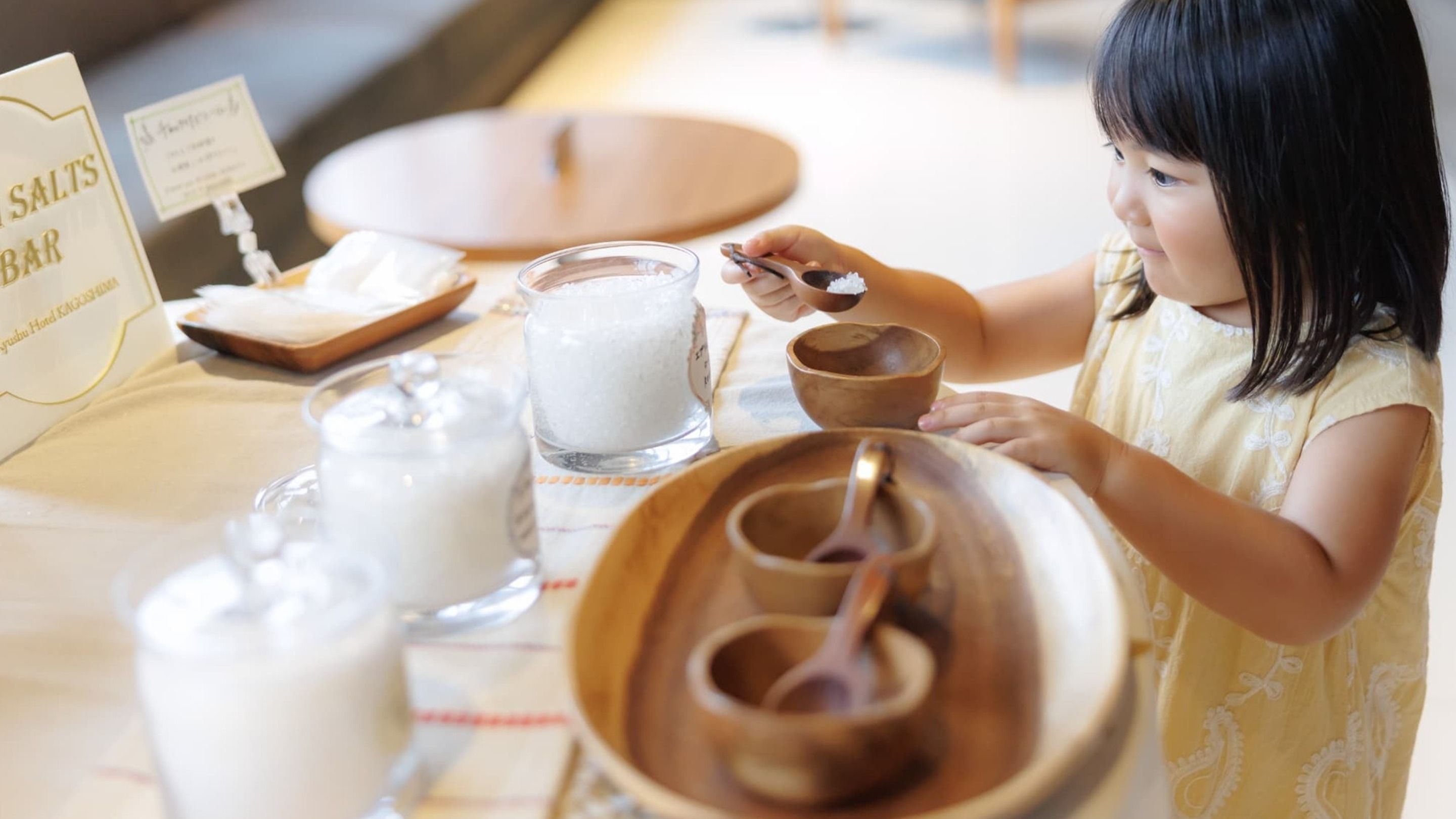 Un bambino seduto a tavola con un saliera, un bicchiere di latte e una ciotola di legno.