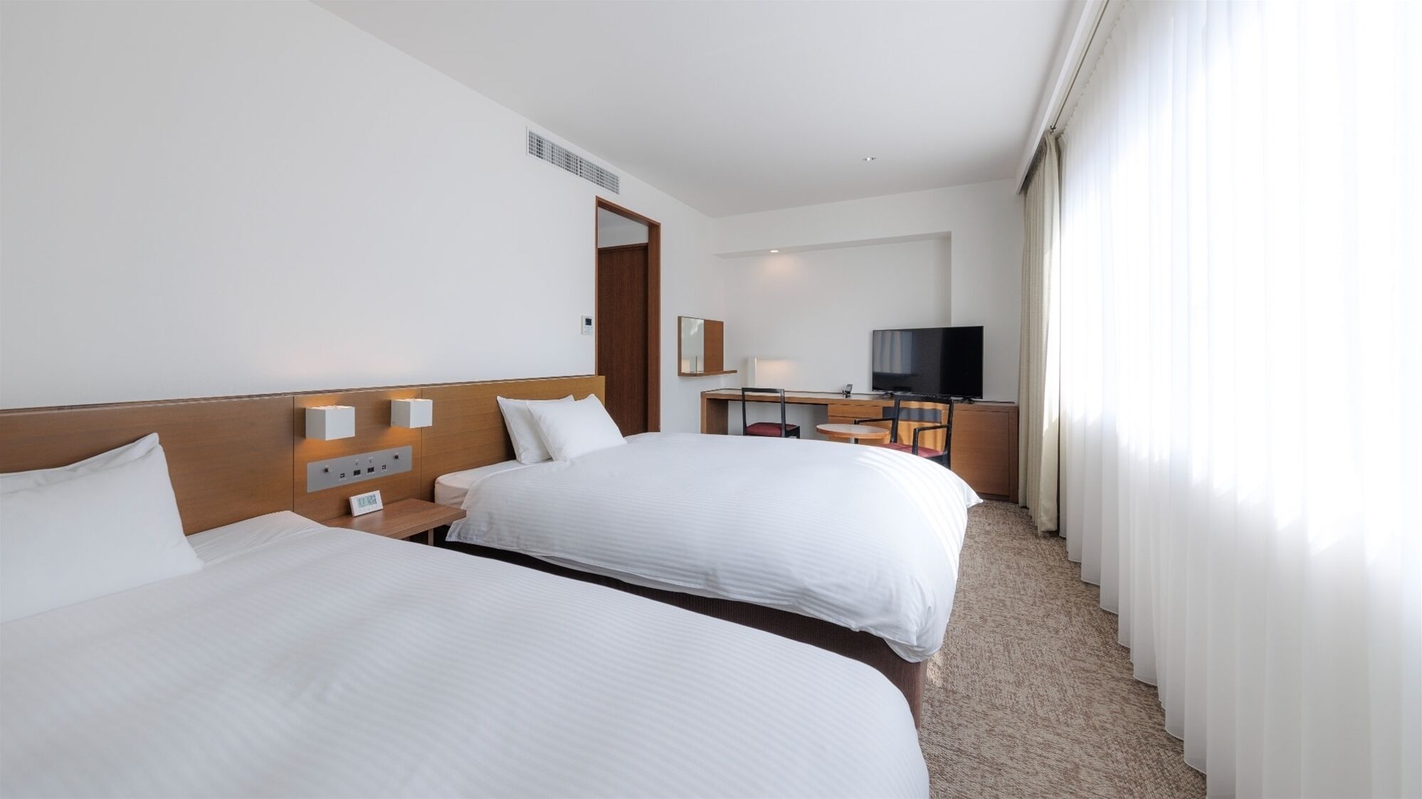 Habitación de hotel con dos camas, un escritorio, una silla, un televisor y una ventana con cortinas.