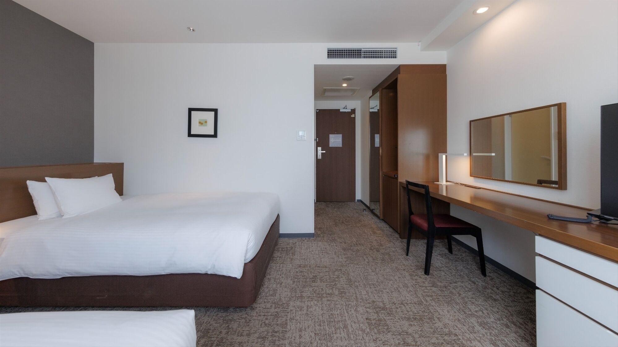 A hotel room with a bed, a desk, a chair, a large mirror, and a door leading to another room.