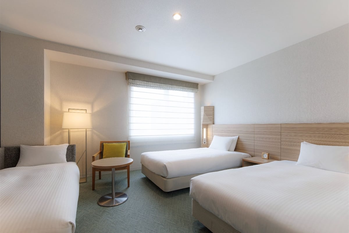 A hotel room with two beds, a small table, and a chair.