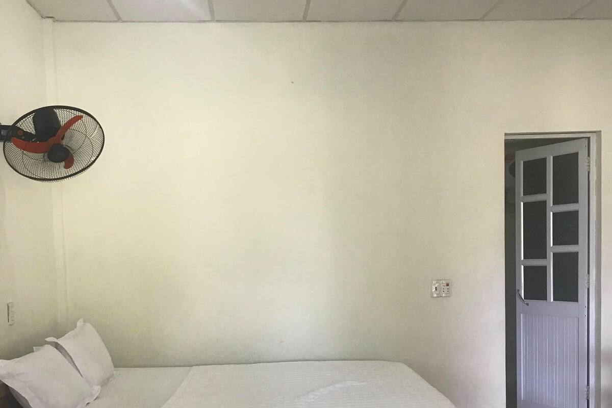 A room with two beds, a standing fan, and a door.