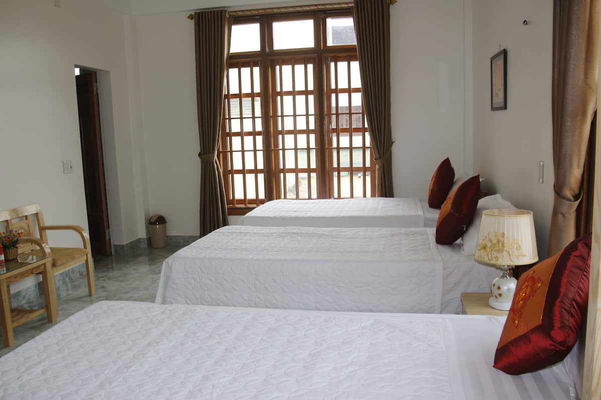 A hotel room with two beds, a wooden chair, a nightstand with a lamp, and a window with curtains.