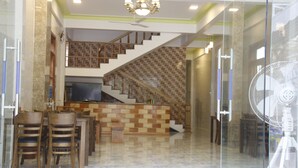 A spacious living area with a staircase, a dining area with wooden chairs, and a fan.