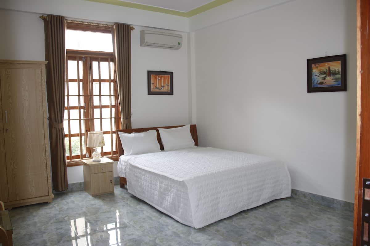A bedroom with a bed, a wardrobe, a nightstand, a window with curtains, and a wall-mounted air conditioner.