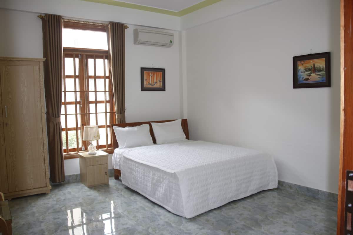 A bedroom with a bed, a nightstand, a wardrobe, a window with curtains, and a wall-mounted air conditioner.