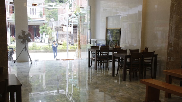 A spacious room with a polished marble floor, a dining area with wooden furniture, and a large window offering a view of the street outside.