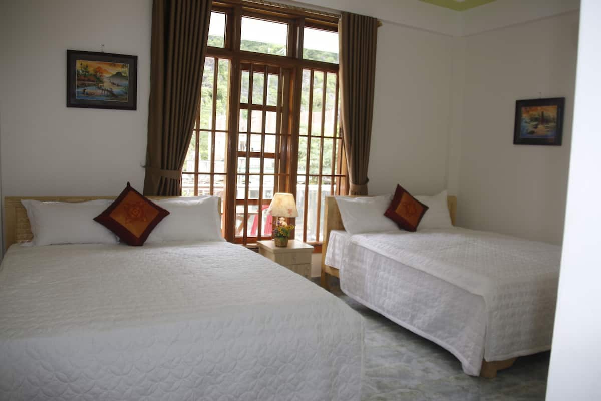 A room with two beds, a nightstand with a lamp, and a window with curtains.