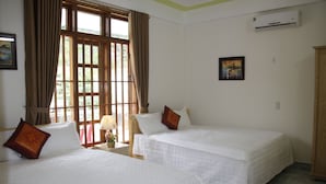 A hotel room with two beds, a window with curtains, an air conditioner, and a framed picture on the wall.