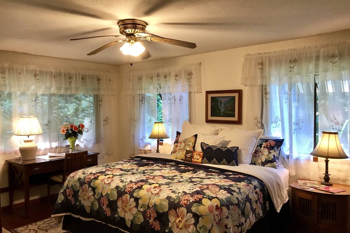 A bedroom with a bed, two bedside tables, a ceiling fan, and floral curtains.