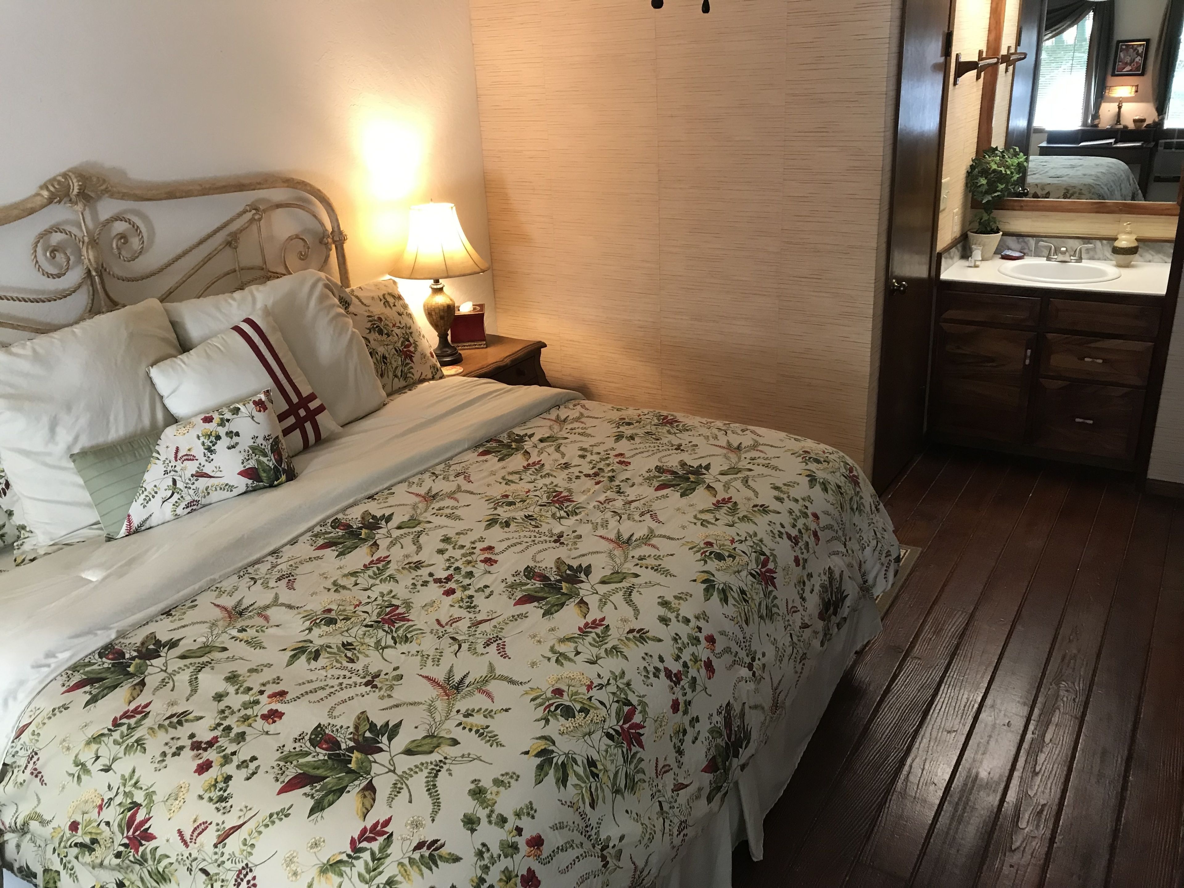 A neatly made bed with floral bedding, a bedside lamp, and a wooden nightstand.