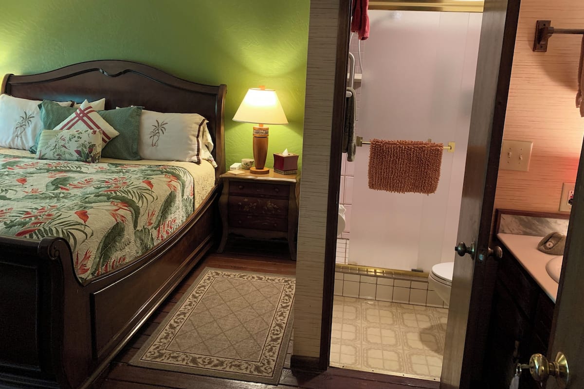 A bedroom with a bed, bedside table, lamp, and a bathroom with a shower and toilet.
