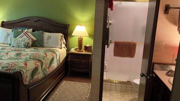 A bedroom with a bed, bedside table, lamp, and a bathroom with a shower and toilet.