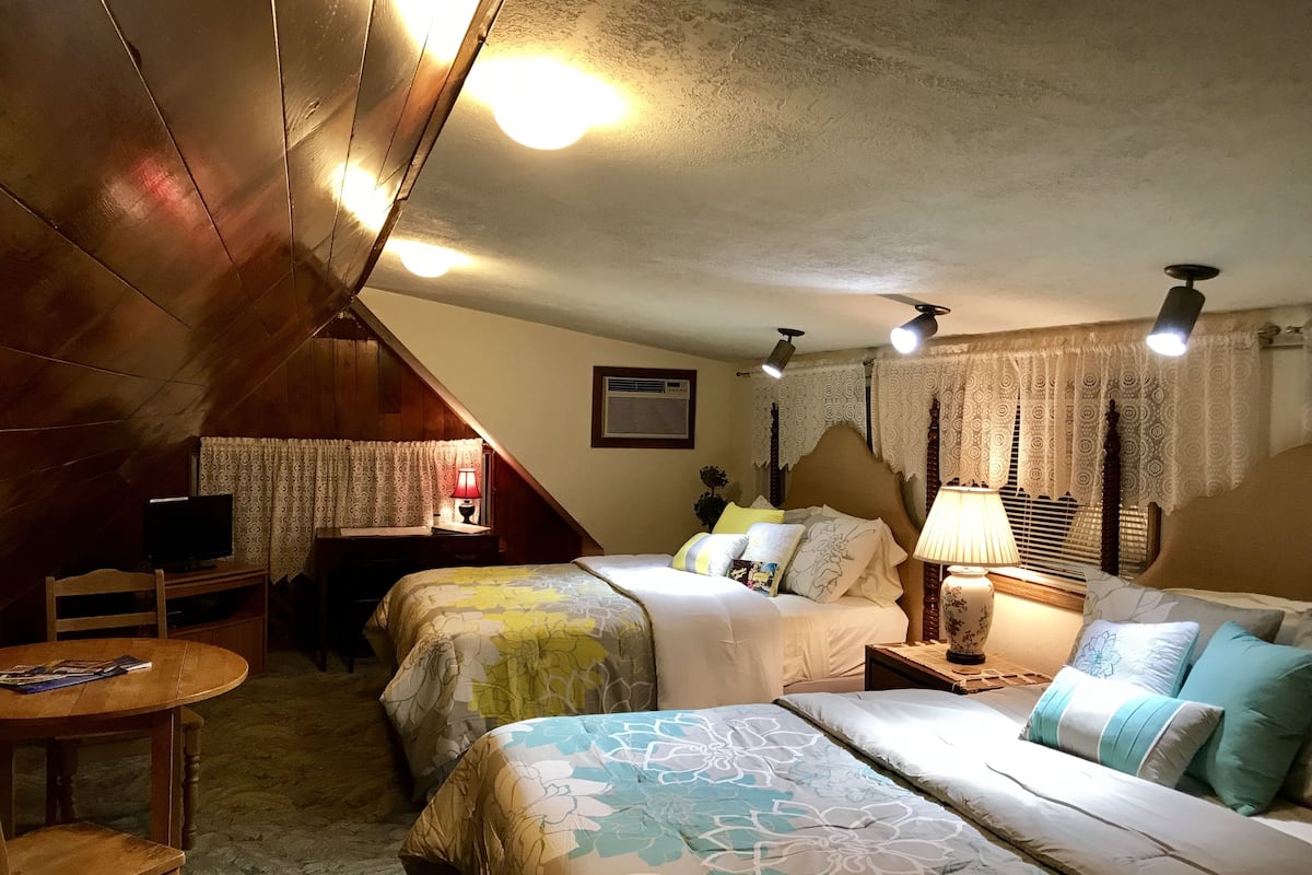 A cozy attic bedroom with two beds, a desk, and a television.