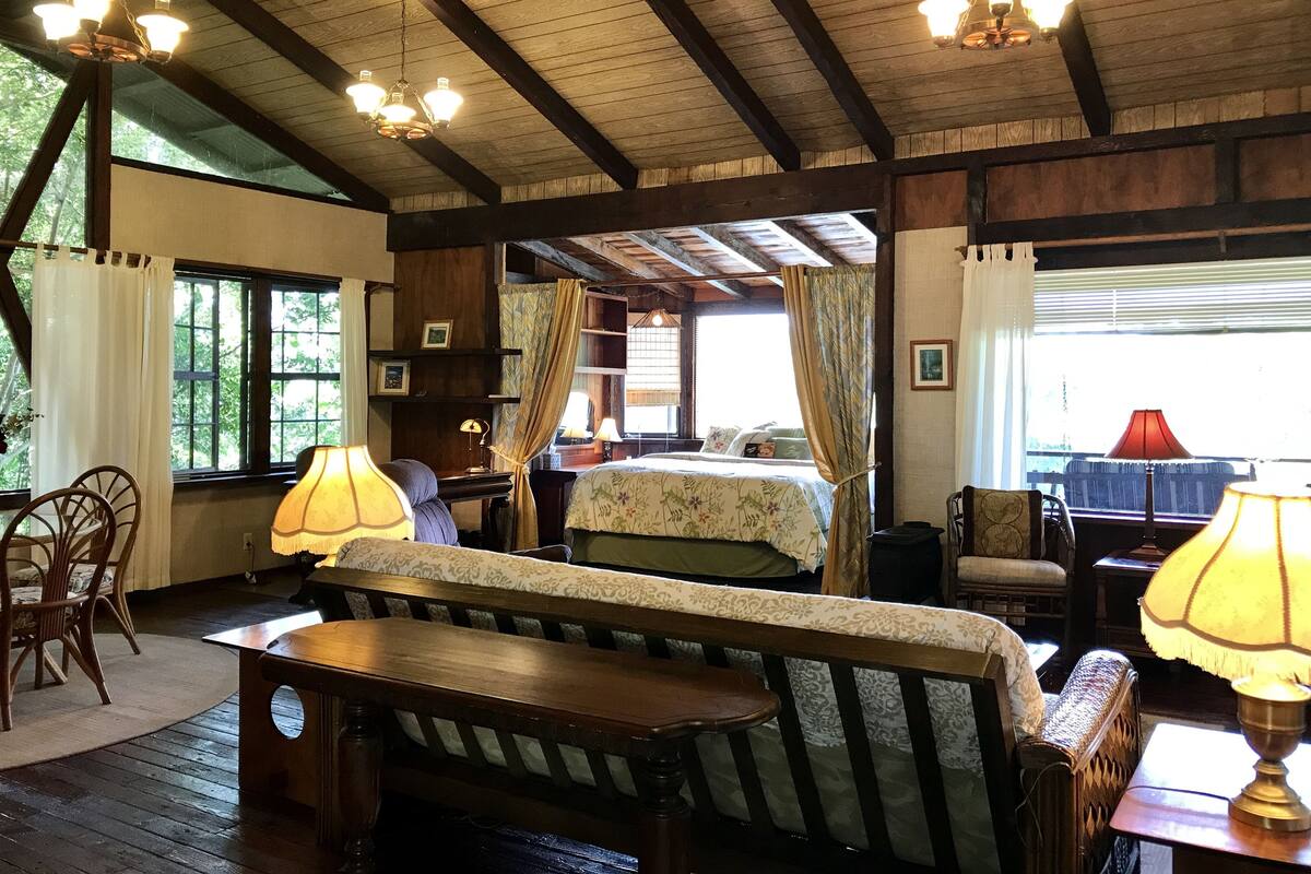 A cozy room with a wooden ceiling, a bed with floral bedding, a desk with a lamp, and a chair.