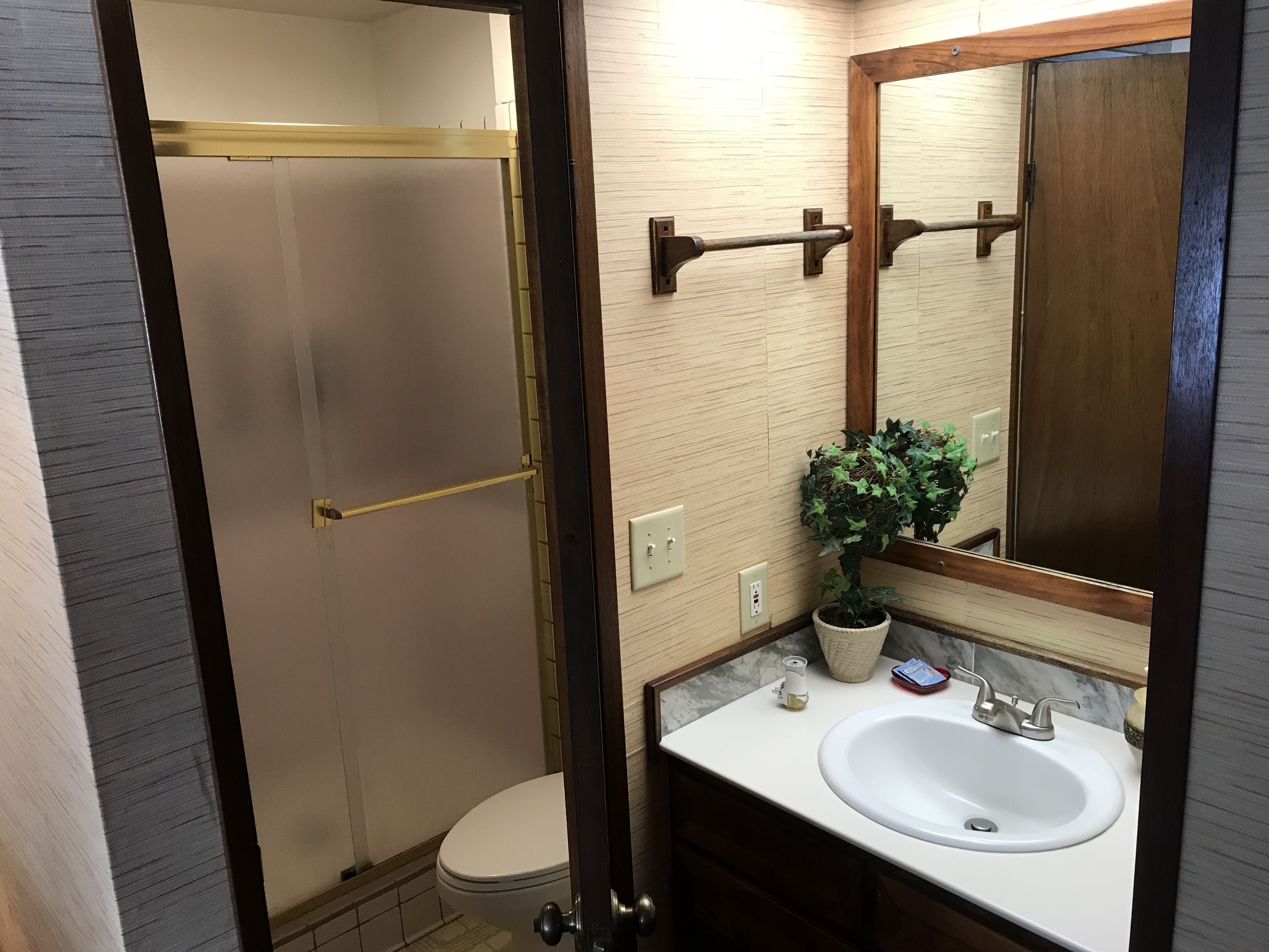 A bathroom with a toilet, sink, mirror, and a shower area.