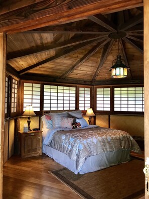 Quarto de madeira com uma cama grande, duas mesas de cabeceira e um lustre.