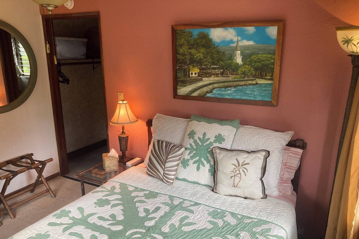A neatly arranged bedroom with a bed, pillows, a nightstand, a lamp, a painting, and a window.