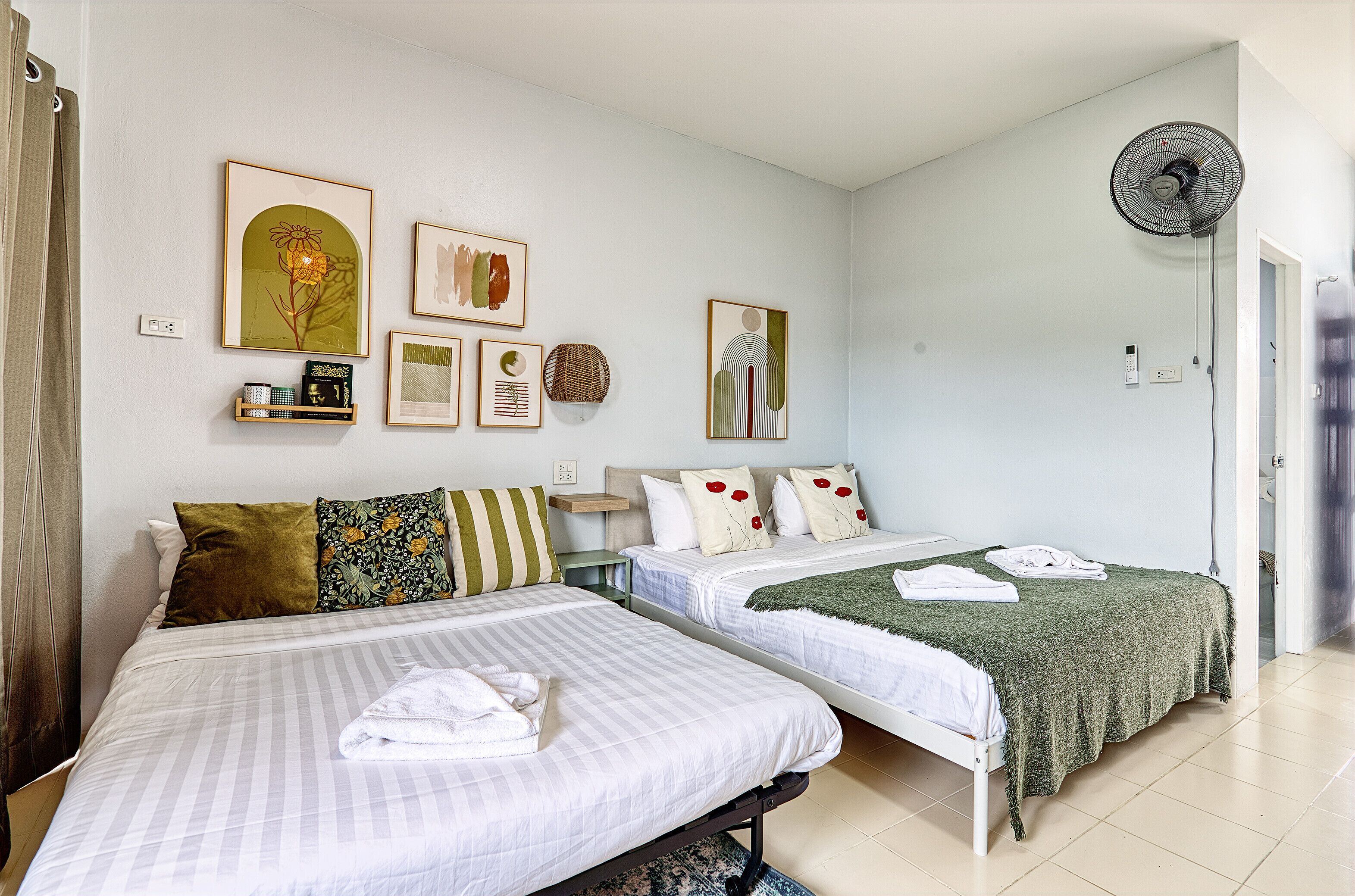 Habitación de hotel con dos camas, un ventilador de pie y decoración en la pared.