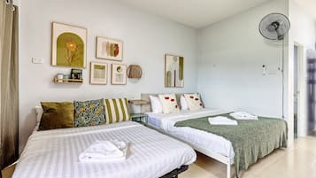 Habitación de hotel con dos camas, un ventilador de pie y decoración en la pared.