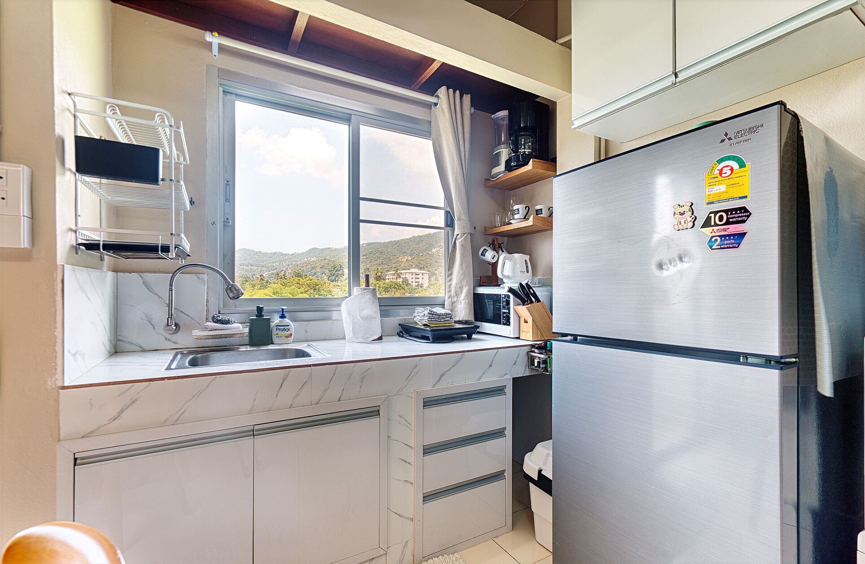 Una cocina moderna con un refrigerador de acero inoxidable, una ventana con vistas a las colinas, un fregadero y una encimera con diversos utensilios de cocina.