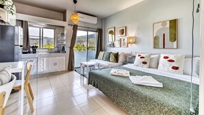 Una habitación de hotel moderna con kitchenette, zona de comedor, sofá cama y un gran ventanal con vistas al exterior.