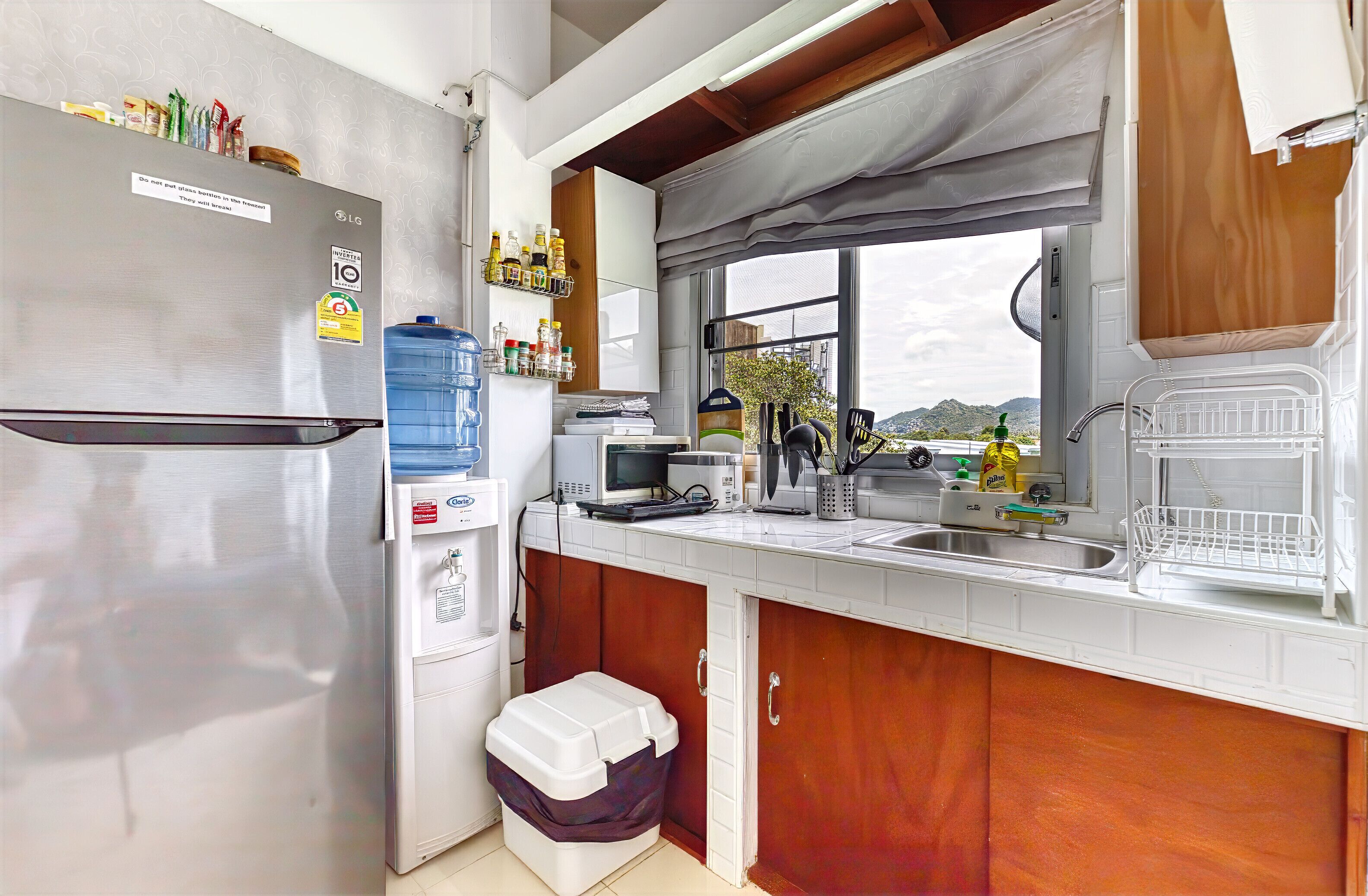 Una cocina compacta con refrigerador de acero inoxidable, microondas, lavamanos y ventana con vista al exterior.