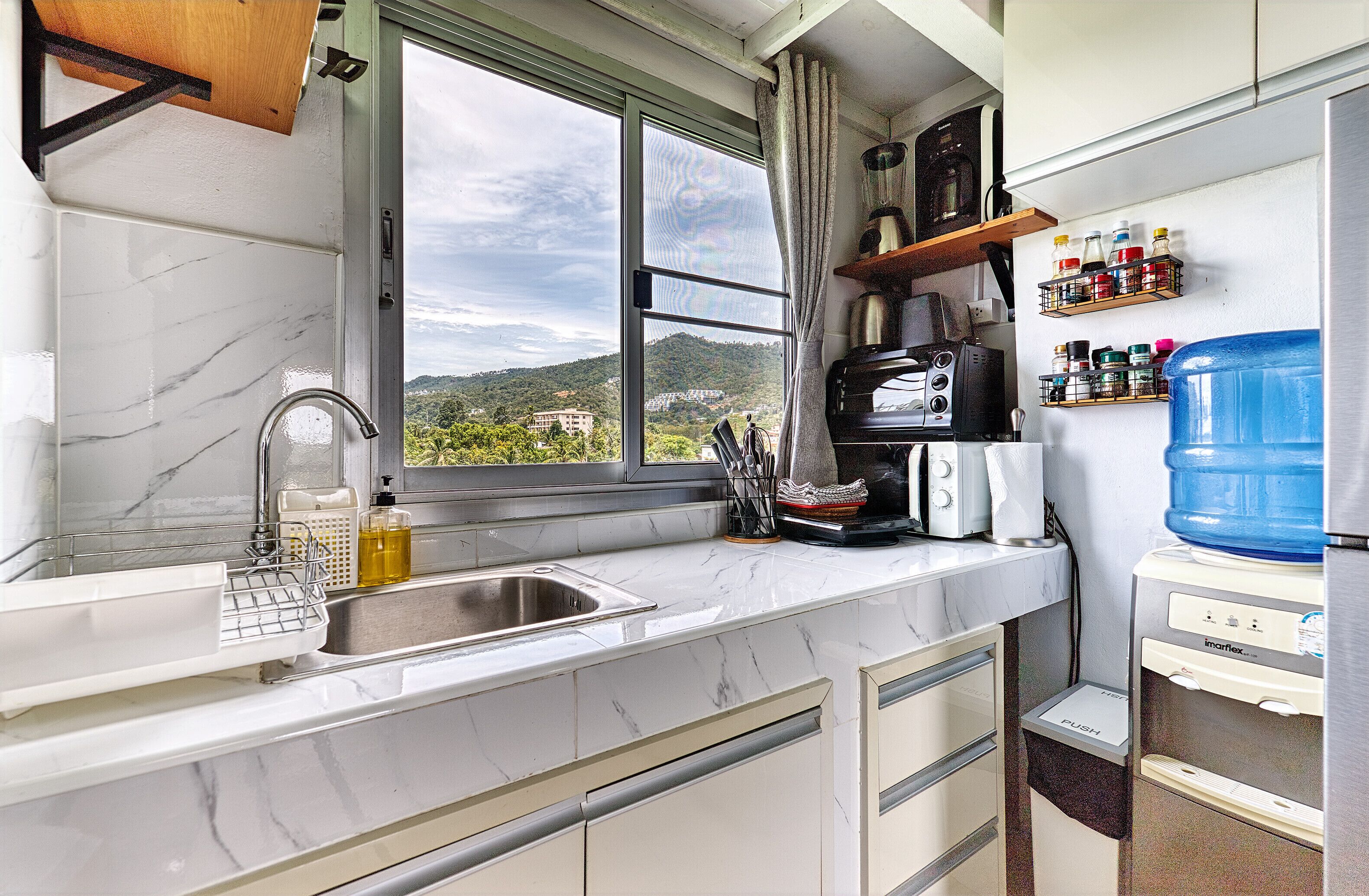 Eine Küche mit großem Fenster, Spüle, Mikrowelle, Toaster und Wasserspender.