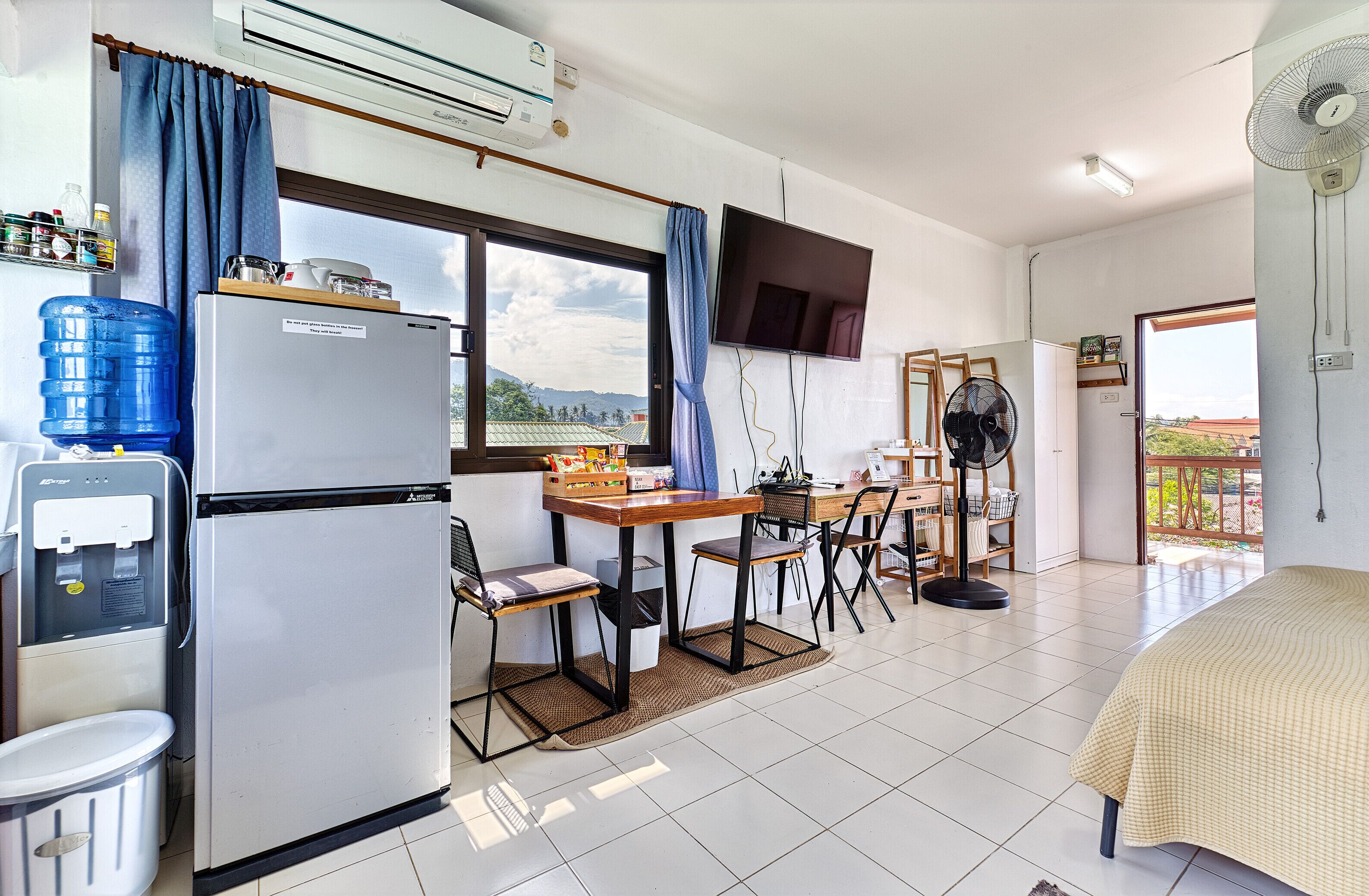 Habitación de hotel compacta con kitchenette, un amplio ventanal con vistas, televisor de pantalla plana y balcón con ventilador.