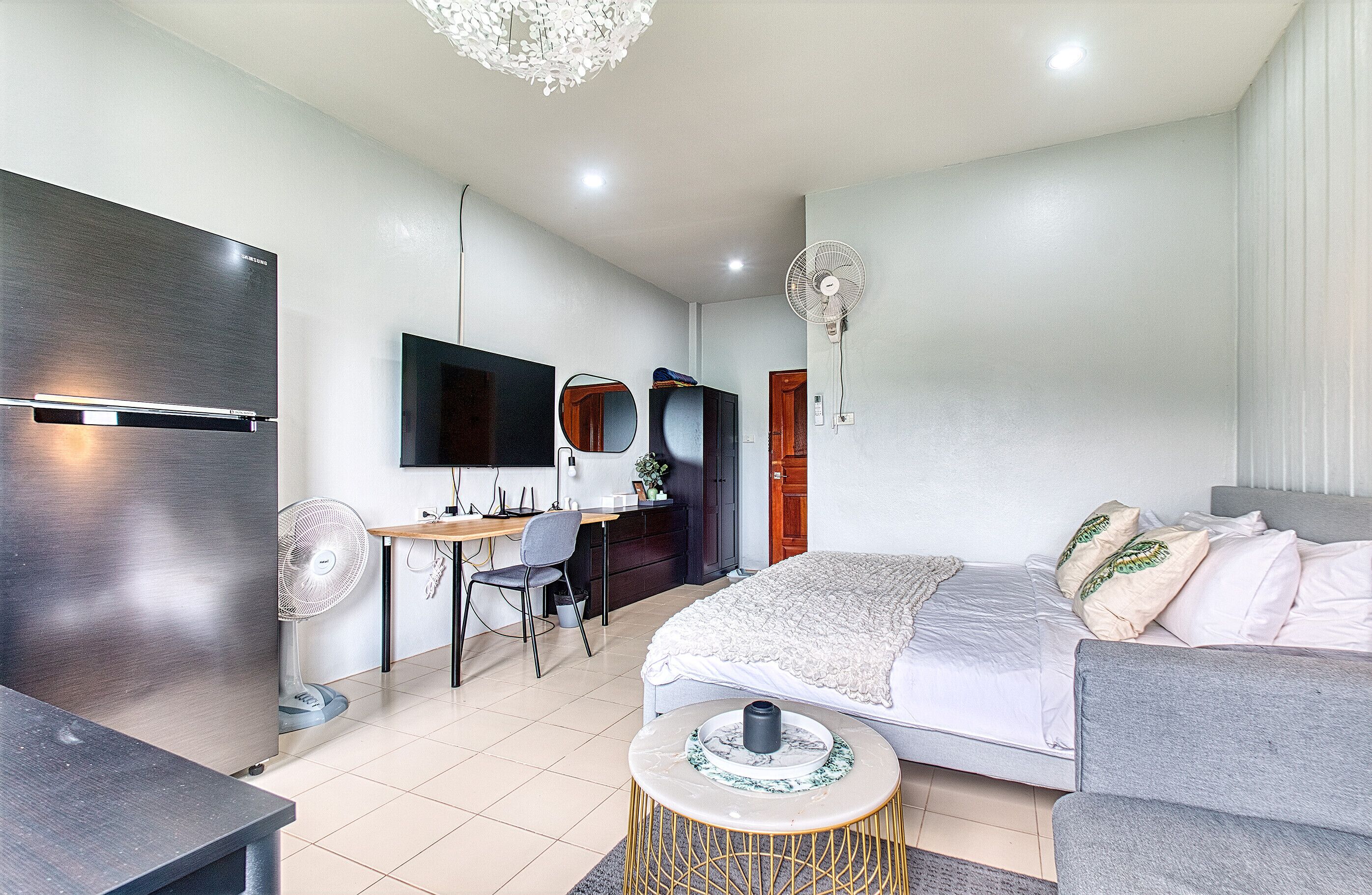 A modern bedroom with a bed, a desk, a chair, a TV, and a fan.