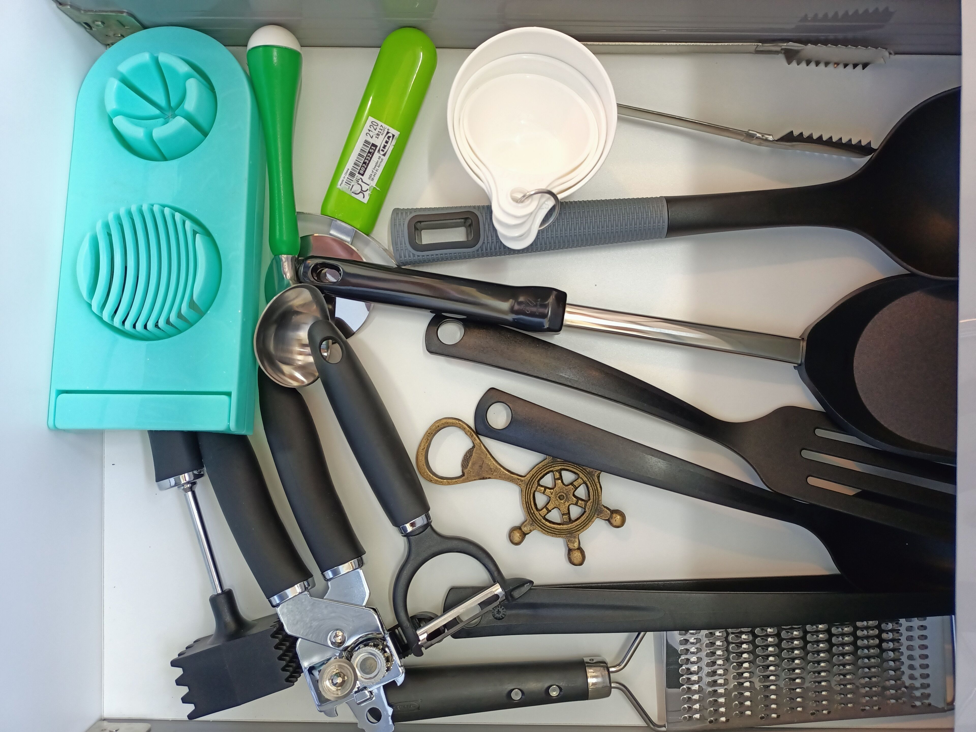 Un cajón con varios utensilios de cocina, incluyendo un rallador, espátulas y un utensilio verde.