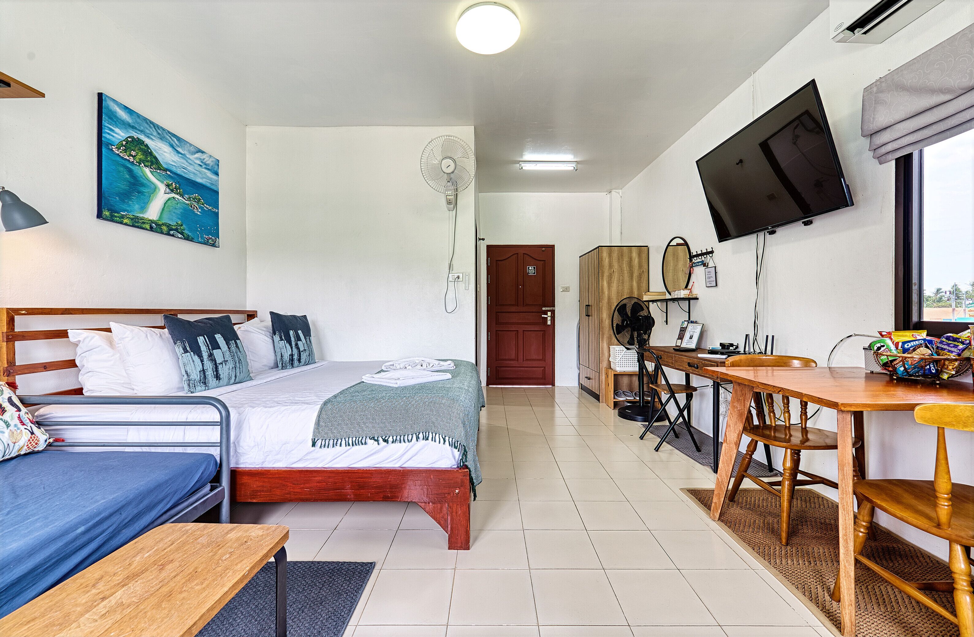 A room with a bed, a desk, a chair, a television, and a fan.