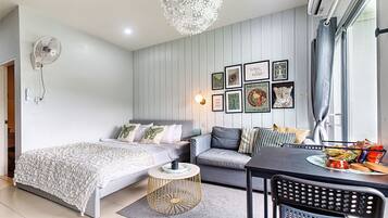 Un dormitorio moderno con cama, sofá, mesa de comedor y ventilador de pared.