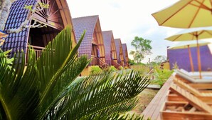 A row of modern, multi-tiered buildings with a sloped roof, surrounded by lush greenery and a wooden deck. - Bataran Garden Cottage (Penida Island)