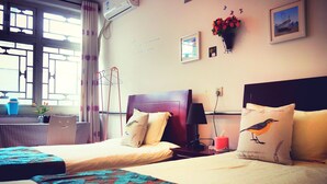 A hotel room with two beds, a window with curtains, a wall-mounted air conditioner, a lamp, and a framed picture. - Beijing Badaling Great Wall Caos Hostel (Yanqing)