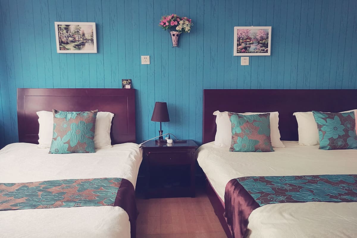 Habitación de hotel con dos camas, una mesita de noche con lámpara y dos cuadros en la pared.