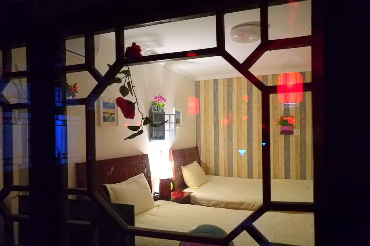 Una habitación con dos camas, un ventanal de estructura geométrica, una flor colgante y un pared a rayas.