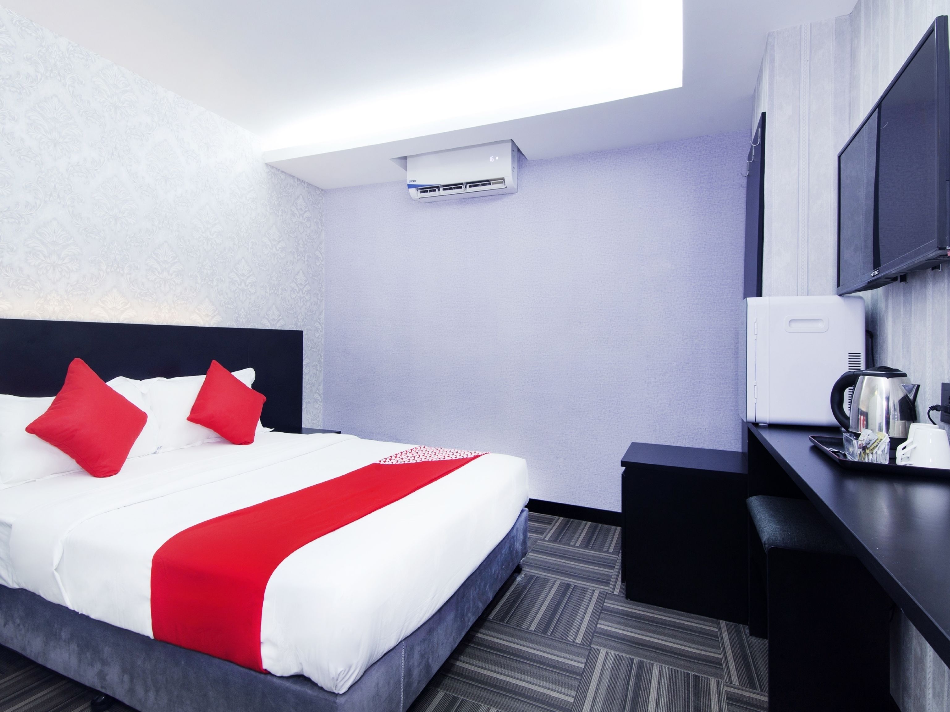 Una camera d'hotel moderna con un letto rifatto, una scrivania con un bollitore e una televisione a schermo piatto fissata al muro.
