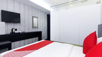 A modern hotel room with a large bed, a flat-screen TV, a small desk with a kettle, and a wardrobe.