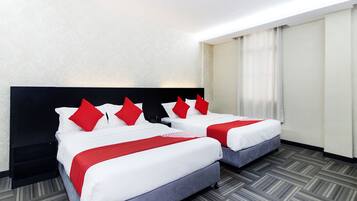 Habitación de hotel con dos camas, cada una con ropa blanca y almohadas rojas, un cabecero negro y una alfombra gris.