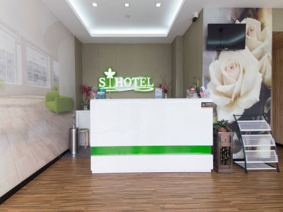 A hotel reception area with a modern design, featuring a reception desk, a green accent strip, a large floral wall mural, and a mounted television.