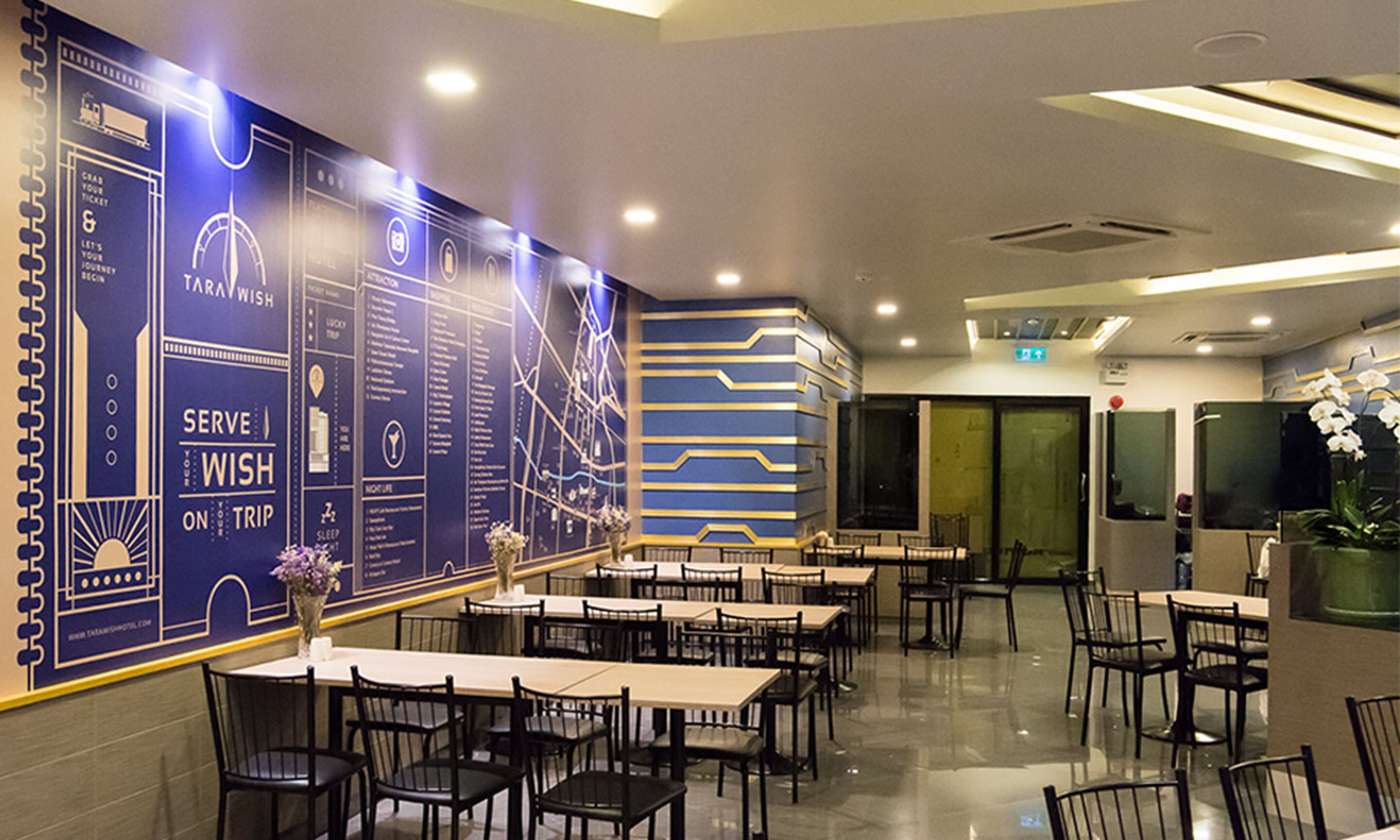 A modern restaurant with a blue and gold color scheme, featuring a wall with a travel-themed design and multiple tables and chairs.